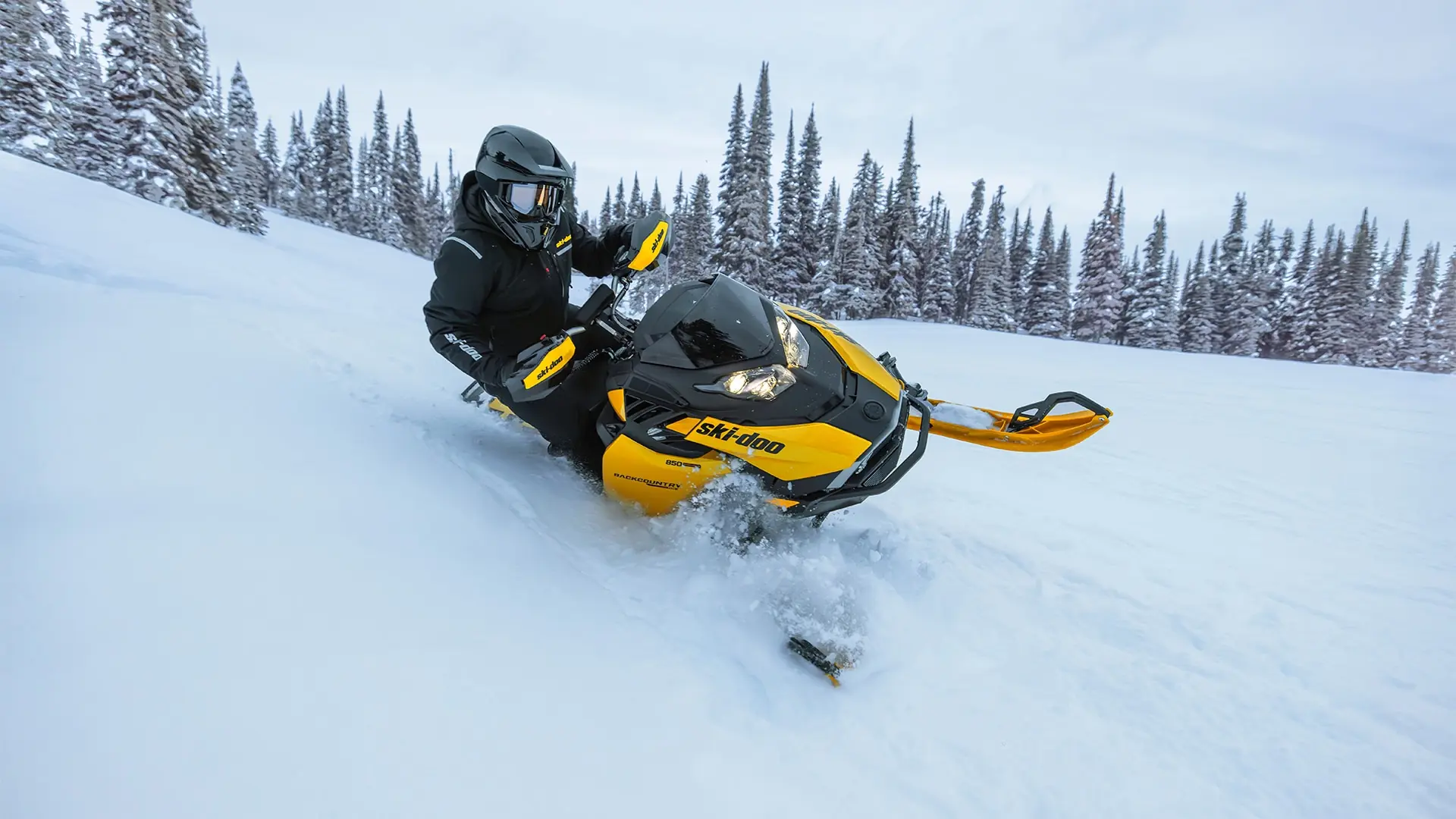 Ski-Doo-snöskoter lutad i djupsnö framför granskog